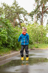 Toddler boy jumping in a puddle in yellow waterproof boots. Fun on the street. Tempering in summer....