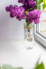 Vertical photo of lilac in a glass vase on a windowsill near the window