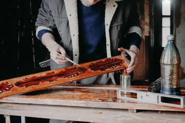 artisan is varnishing a wooden board of a cabinet from solid wood. Work in the workshop restoration.