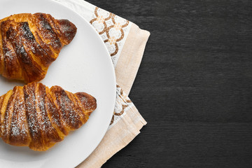 Freshly baked plain croissants on a white plate near serviette on a black wooden background. Homemade french pastry with copy space