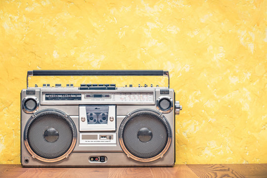 Retro outdated portable stereo boombox radio receiver with cassette recorder from circa 80s front concrete textured yellow wall background. Listening music concept. Vintage old style filtered photo 