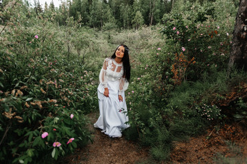 Fairy-tale Princess in a light summer white dress is walking along a wide path towards the wind, a graceful dancing girl in the form of a flower with a fluttering long hem of her dress