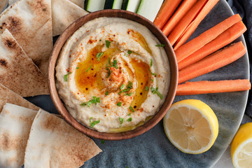Homemade hummus with olive oil, herbs and paprika in a wooden bowl. with vegetable and bread dips.