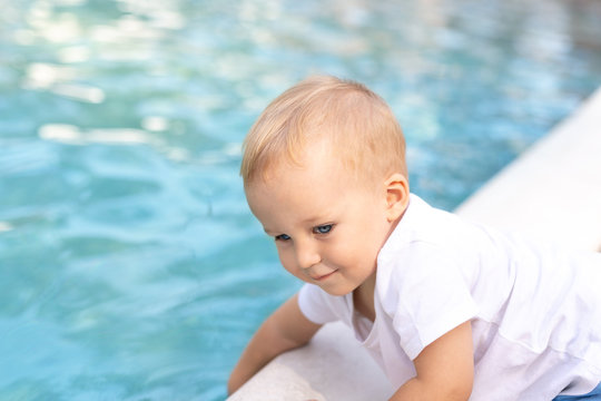 Cute adorable little caucasian blond smiling todller boy kid treing water temperature pool edge before swimming. Happy child wear white t-shirt near poolside enjoy summer vacation travel with family