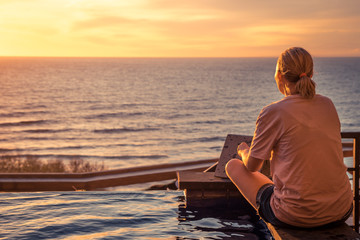 Fototapeta premium Young pensive woman looking at horizon with hope during travel vacation in warm orange colors at sunset over sea