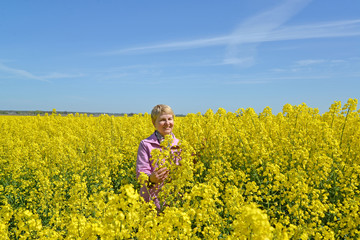 Fototapeta premium Middle-aged woman stands in flowering rapeseed field