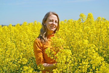 Young woman stands in flowering rapeseed field