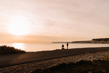 dad walks with a stroller by the sea at sunset, silhouette