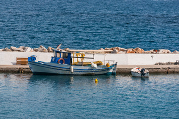 Obraz premium An old fishing ship and a motor boat at the pier against the background of the blue sea.