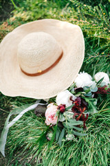 A woman's summer hat and a wedding bouquet made of eucalyptus and English roses lie on a green grass backround. The concept of a modern wedding