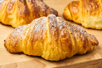 Close up three freshly baked croissants with sugar powder on a wooden desk. Puff french pastry. 