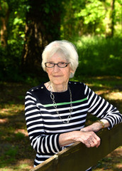 Elderly Woman Leans on Wooden Fence