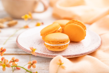 Orange macarons or macaroons cakes with cup of apricot juice on a white wooden background. Side view, selective focus