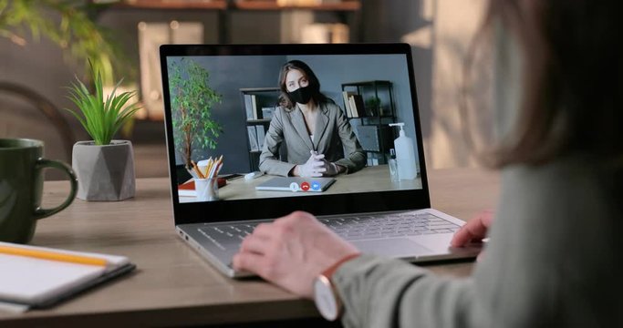 Woman having online business conference with female boss in mask in lockdown. Businesswoman talking on video call with employee while sitting in cabinet at office. Video chat. Quarantine concept