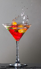 Yellow maraschino cherry spalshing into glass of vodka filled with other cherries