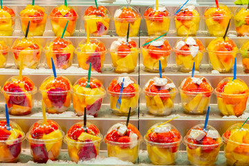 Fruit salad cups of fresh colorful cut/ sliced fruits on store shelf display. Farmers Market local agricultural produce, healthy raw vegan/ vegetarian dish. Delicious packaged lunch snack for sale.