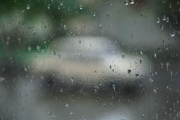 Window overlooking a rainy street. Gloomy evening weather with a view of the road. Drops on glass and bokeh from cars. Stock background for design