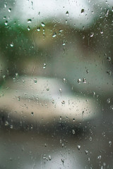 Window overlooking a rainy street. Gloomy evening weather with a view of the road. Drops on glass and bokeh from cars. Stock background for design