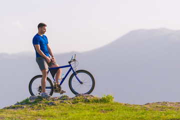 Obraz premium Fit mountain biker riding his bike through green grass on top of a mountain.
