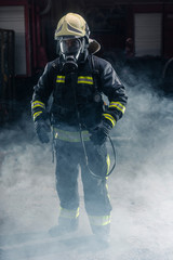 Obraz premium Portrait of a fireman wearing firefighter turnouts and helmet. Dark background with smoke and blue light.