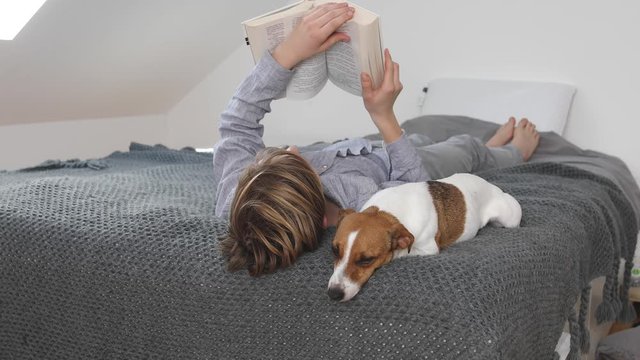 Boy reading a book lying with his dog on bed at home