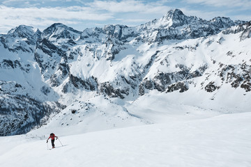 Man climbing a mountain with skies on a panoramic slope in the alps in a sunny day