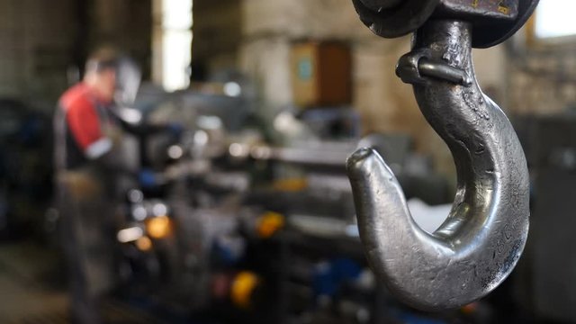 Heavy industry concept. Steady shot of suspended crane working at factory. Metal crane hook hanging Inside Industrial Factory. Plant Interior with blurred Equipment and readymade details in disfocus