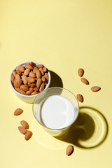 Almond milk in a glass on yellow background - alternative dairy