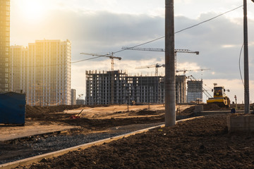 Silhouettes of tower cranes and builders in action on sunset background. Workers during formwork and pouring concrete through a сoncrete pump truck connected to a ready-mixed truck. Concrete pumping