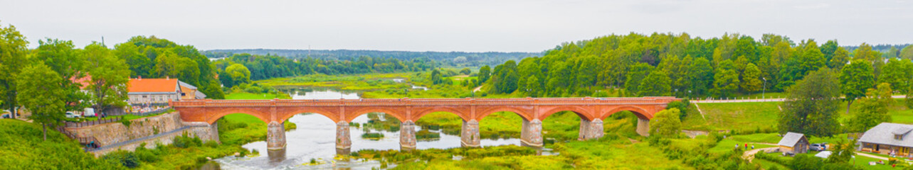 Fototapeta na wymiar Beautiful panoramic aerial view photo from flying drone to Venta Rapid waterfall,the widest waterfall in Europe and the third longest brick bridge in Europe on a summer day in Kuldiga, Latvia.(series)