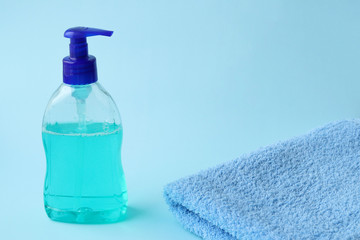 Fototapeta na wymiar Liquid soap in a plastic bottle with a dispenser and a folded blue towel on a blue background. Selective focus. Hand and body hygiene. Antibacterial soap. Prevention of coronavirus.