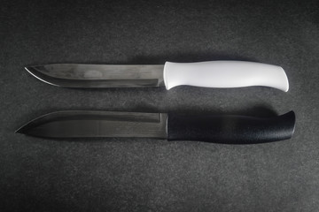 Two kitchen knives with white and black handles on a dark background.