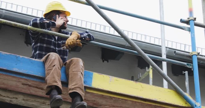 Construction worker sitting on scaffold making phone call