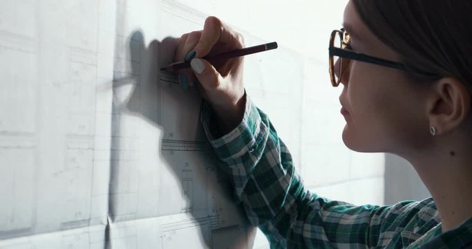 Close-up portrait of beautiful woman concentrated on work. Architect working in office with blueprints. Engineer sketching a construction project. Architectural plan. Business construction concept.