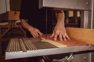 a male carpenter cutting wooden plank on the band saw in workshop, closeup