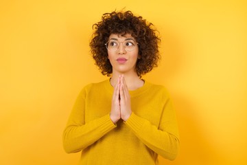 Young Arab woman against a yellow background wearing yellow sweater making up plan in mind holding hands together, setting up an idea.