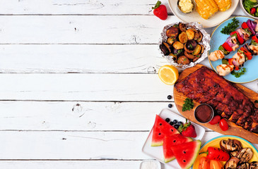 Summer BBQ or picnic food side border. Selection of grilled meat, vegetables, fruits and potatoes. Top down view over a white wood background. Copy space.