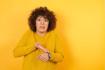 Young arab woman with curly hair wearing yellow sweater  standing over isolated yellow background...