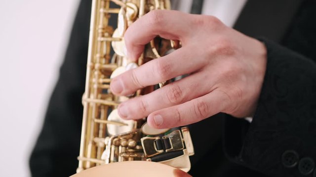 Person performs song in recording studio. Man holds saxophone. Person wears dark suit and white shirt.