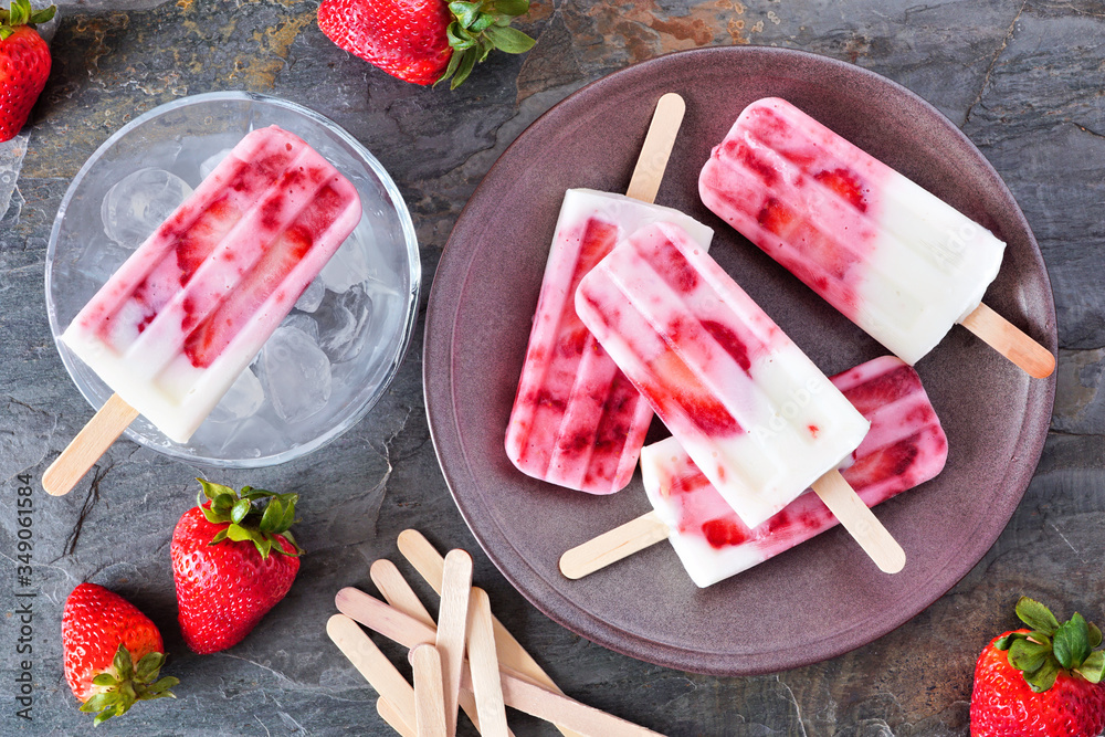 Poster strawberry vanilla yogurt ice pops. top down table scene with a dark stone background.