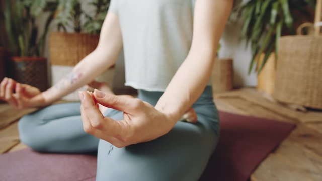 Close up shot of unrecognizable barefoot woman in sportswear sitting in lotus pose on mat and holding hands in mudras during yoga practice at home