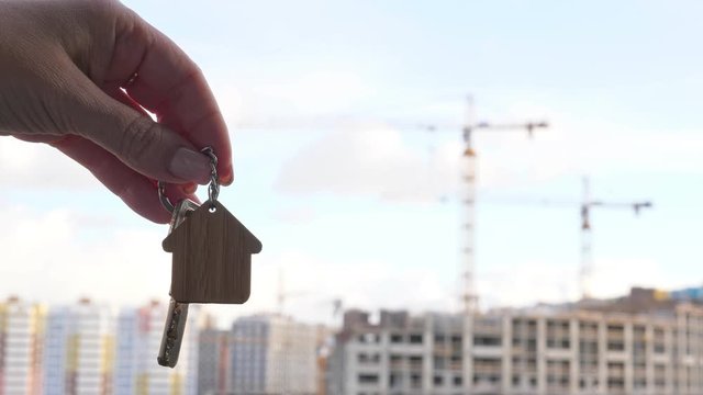 Key with house keychain in hand on background with new high-rises houses construction. House purchase and real estate concept