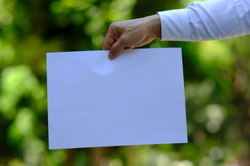 hand holding a white paper on green background