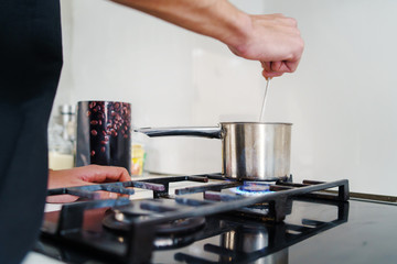 Close up on male hand caucasian holding a metal shiny spoon mixing while cooking in pot homemade black coffee in kitchen at home in day