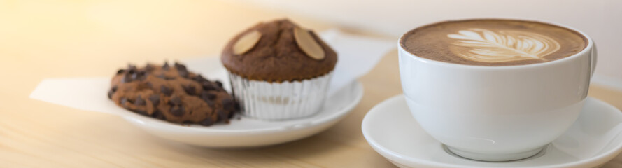 Closeup of white cup of hot coffee latte with milk foam art with muffin and chocolate chips cookie on wooden table use for cover page concept.