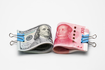 Two stacks of rolled up one hundred US dollar and Chinese  Renminbi yuan banknotes clamped with paper clips on white background. Concept of saving, cooperation, confrontation, decoupling.