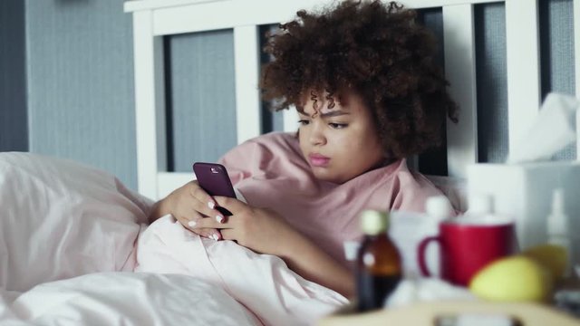 Sick Young african american girl using phone in bed at home