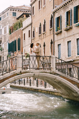 Fototapeta na wymiar Italy wedding in Venice. The bride and groom are standing on a stone bridge over a narrow Venetian canal. Newlyweds walk around the city taking pictures on the street.