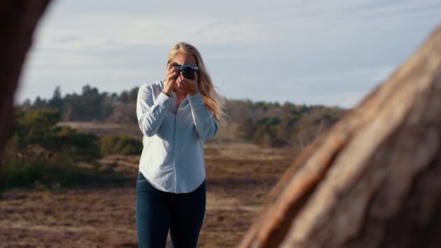 Facing a blonde woman, brings a camera to her eye to take a photo, slow motion