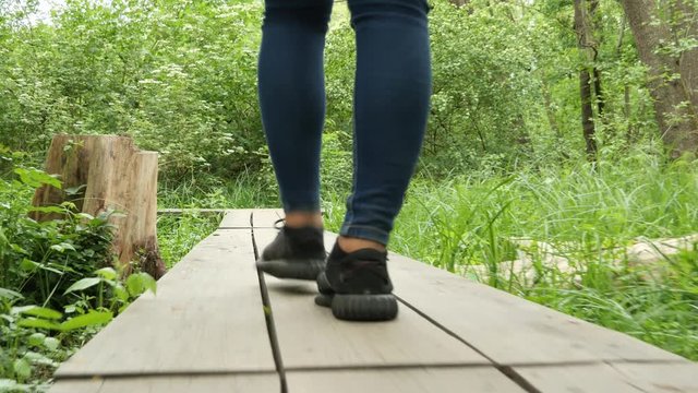 A Young Woman walking on a Boardwalk in a Forest next to a Swamp Area, Filmed Low to the Ground